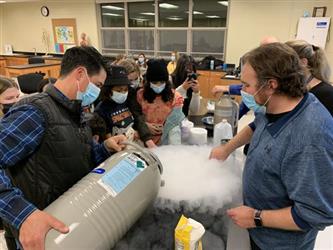 Teachers and students gather around a canister of dry ice being poured on a science lab table