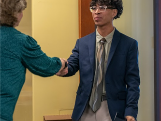 A business tech student in formal business attire shaking an adults hand