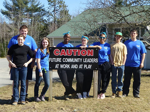 Students gather by a sign that reads caution: future community leaders at work and play